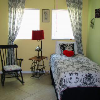 Cozy bedroom with a single bed, rocking chair, and bright natural light from the windows.
