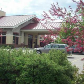 A building with a car parked in front, surrounded by trees and bushes.