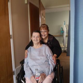 A caregiver smiling while assisting an elderly woman in a wheelchair.
