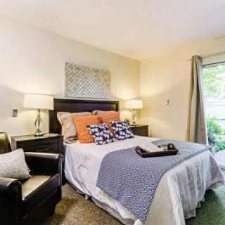 A modern bedroom with a comfortable bed and cozy armchair, featuring stylish decor and ample natural light.