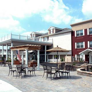 A spacious outdoor patio area with tables and chairs, set against a large residential building under a blue sky.