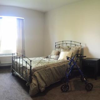 A cozy bedroom with a bed, pillows, and a walker next to the nightstand.