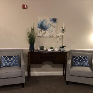 A cozy seating area with two gray chairs, accent cushions, and a decorative console table adorned with plants and artwork.