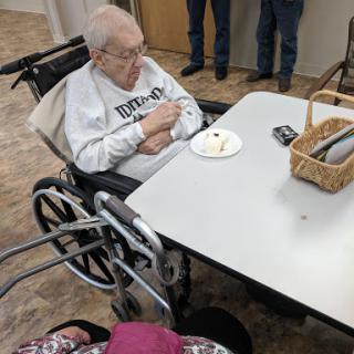 An elderly person enjoying dessert at a social gathering in a care facility.