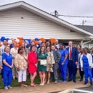 A group of people posing for a photo outside in front of a house with balloons in the background.