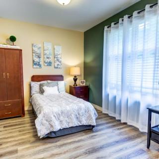 A cozy single bedroom with modern decor, featuring a large window with sheer curtains and wooden flooring.