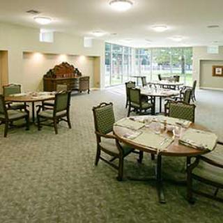 A spacious dining room with round tables and chairs, featuring a carpeted floor.