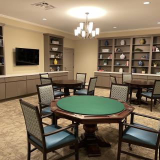 A cozy game room featuring a poker table surrounded by chairs, with a television and built-in shelves in the background.