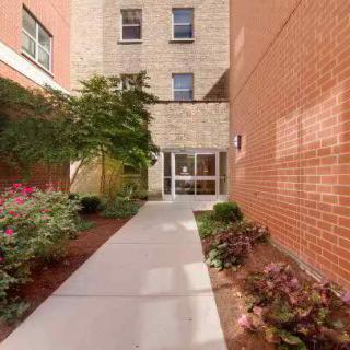 A landscaped pathway leading to the entrance of a building with brick and stone exterior walls.