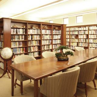 A cozy library with bookshelves, a large wooden table surrounded by chairs, and decorative items such as a globe and a bonsai plant.
