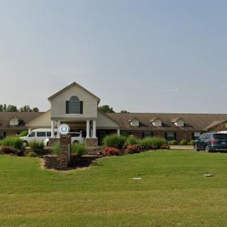 A large residential or institutional building with well-maintained landscaping and parked vehicles on a sunny day.