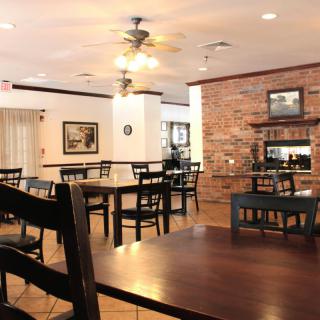 A cozy restaurant interior with wooden tables and chairs, brick wall, and ceiling fans.