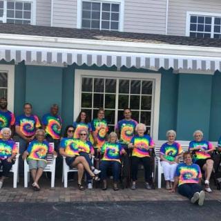 A group of people wearing colorful tie-dye shirts gather for a casual outdoor photo.