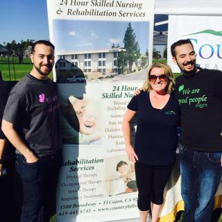 Three people smiling in front of a promotional banner at an outdoor event.