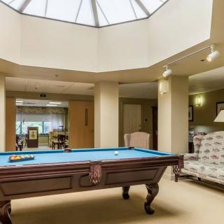 A spacious room featuring a billiards table under a skylight, with comfortable seating and soft lighting.
