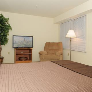 A cozy bedroom with a bed, chair, TV, and lamp.