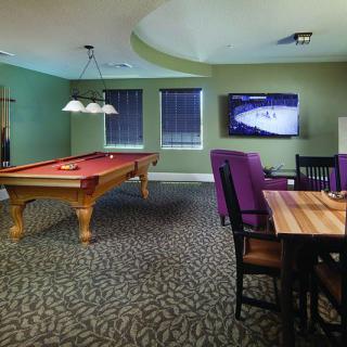 A cozy game room featuring a pool table, wall-mounted television, and a small dining area with purple chairs.