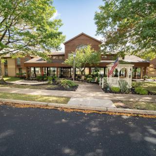 A front view of a building with a well-maintained garden and pathway, surrounded by trees during the daytime.