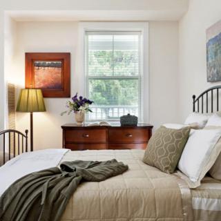A cozy bedroom with a neatly made bed, soft lighting, and a view through a window.