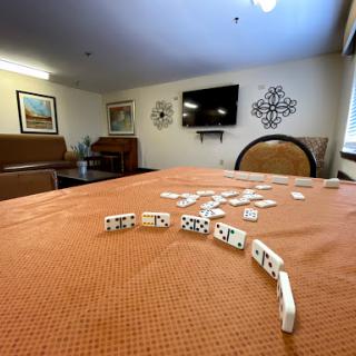 A cozy recreation room featuring a game of dominoes in progress on an orange tablecloth.