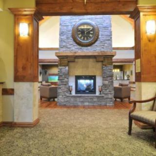 A cozy lobby interior with a central fireplace, surrounded by seating and adorned with a large clock on the stone wall.
