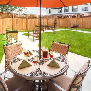 A cozy outdoor dining area with a table and chairs under an umbrella, set in a well-maintained backyard.