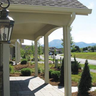 A sunny porch with columns overlooking a landscaped yard and distant mountains.
