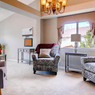 A cozy living room featuring patterned armchairs, a chandelier, and natural light from a large window.