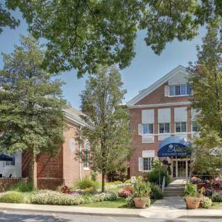 A well-maintained building surrounded by lush trees and landscaping under a clear summer sky.