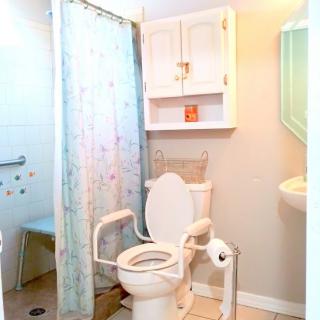 An accessible bathroom featuring a toilet with support rails, a shower area with grab bars, and a sink.