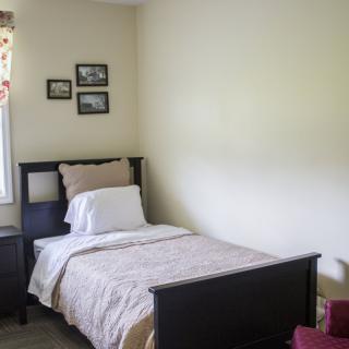 A cozy and simple bedroom with a single bed, nightstand, and pictures hanging on the wall.