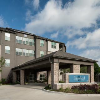 A modern hotel building with a covered entrance and a cloudy sky background.
