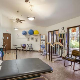 A well-equipped therapy room featuring exercise balls, various chairs, and rehabilitation tools.