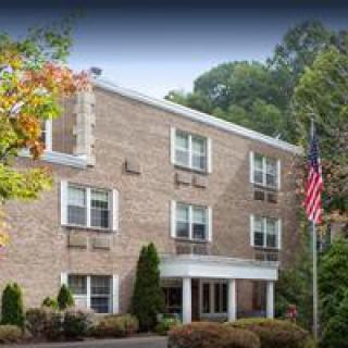 A brick building with multiple windows, surrounded by trees and an American flag in front.