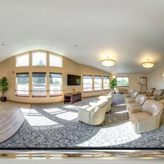 A spacious living room with ample seating, large windows, and a TV, lit by ceiling lights.
