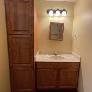 A bathroom vanity with wooden cabinets, a mirror, and overhead lighting.