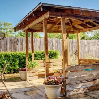 A sunny backyard featuring a wooden gazebo surrounded by potted plants.