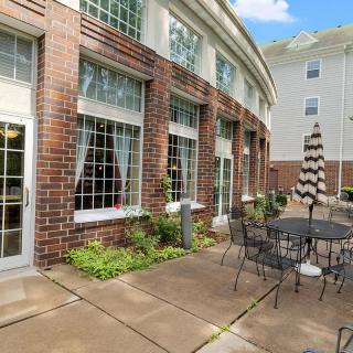 A cozy outdoor patio area with tables, chairs, and an umbrella adjacent to a brick building.