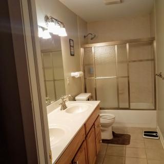 A cozy bathroom with a double sink vanity, glass shower doors, and illuminated mirror.