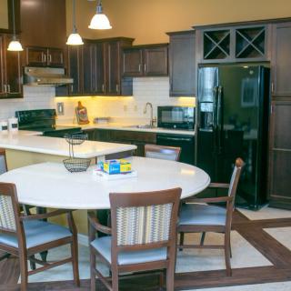 A modern kitchen interior featuring a round dining table, wooden chairs, and sleek dark cabinetry with built-in appliances.