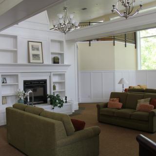 A spacious living room featuring a fireplace, green sofas, chandeliers, and built-in shelves.