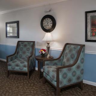 A cozy seating area featuring two patterned chairs, a side table with a lamp, and decorative elements on the walls.