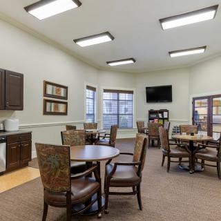 A cozy room with tables and chairs, featuring a kitchenette and a television.