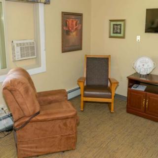 A cozy living room features an armchair, a wooden chair, and wall art.