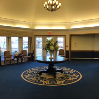A spacious lobby with a round table and floral arrangement under a chandelier.