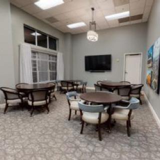A modern conference room with multiple tables and chairs, a wall-mounted television, and decorative artwork.
