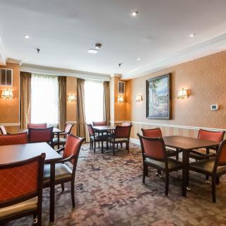 A dining room with several tables and chairs, featuring warm lighting and artwork on the walls.
