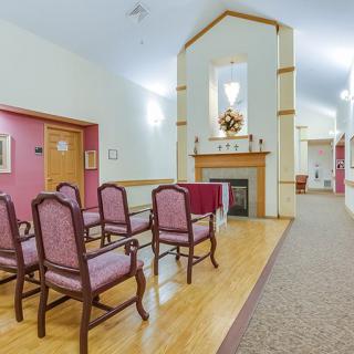 A small chapel room with neatly arranged chairs facing a decorative fireplace.