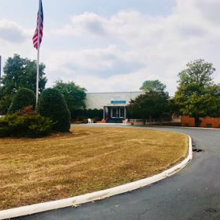 A view of a building with an American flag surrounded by green trees and landscaped grounds.
