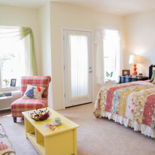 A cozy bedroom with colorful decor, featuring a bed and a chair bathed in natural light.